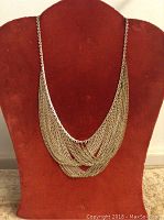 Front view of a gold-tone multi-strand chain necklace displayed on a red velvet bust, showing the draped, layered design typical of 1920s style.