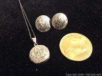 Hand engraved round sterling silver locket pendant on thin chain with matching round sterling silver earrings, placed next to a coin for size reference.