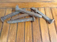 Photo of five rusted railway spikes on a wooden surface, showing their length and flathead tops.