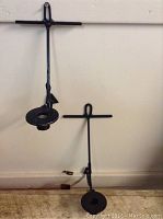 Photo of two black wrought iron anchor-shaped wall candle holders displayed against a white wall, showing front view and hanging hook