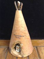 Front view of 8 inch birch bark teepee souvenir with 'ALGONQUIN PARK' inscription, entrance detail with fibrous material and small white object inside.
