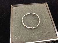 Top view of the thin braided sterling silver ring in its display box, showing the twisted design.