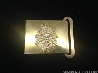 Front view of the metal belt buckle showing the plated military insignia with crossed rifles, anchor, and crown casting a shadow on the polished gold-tone background.