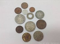 Top-down photo showing 13 old coins in varying conditions and metals arranged on white background.