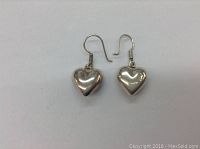 Front view of the pair of sterling silver puffy heart earrings with hooks, showing their polished and rounded shape.