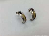 Pair of half hoop stud earrings shown from front angle displaying two-tone Baltic amber inlay in sterling silver frame