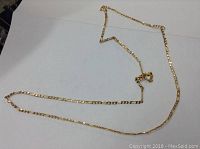 Full view of the 22-inch gold Figaro chain laid out on a white surface showing its length and typical Figaro pattern link design.