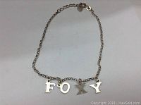 Full view of the silver ankle bracelet with FOXY letter charms spread out flat to show letters and chain structure.
