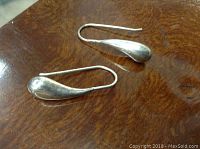 Pair of sterling silver teardrop shaped hanging earrings placed on wooden surface showing smooth polished finish and simple design.