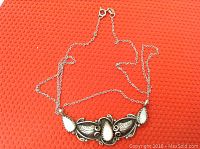 .925 sterling silver chain necklace with ornate antique-style pendant featuring mother of pearl inlays, shown on red textured background.