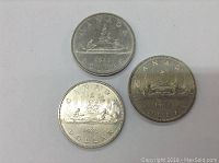 Top side view of three Canadian one dollar coins dated 1982 and 1983 showing the Voyageur canoe design