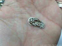 Pendant held in the palm of a hand showing size and detail of the sterling silver flip flop with floral diamond pattern.