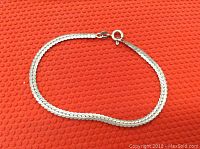 Sterling silver herringbone bracelet laid flat on a textured red surface showing the full length and design of the bracelet.