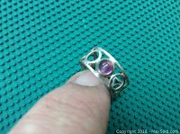 Ring held between fingers showing the front view with pink stone and open circular swirl design on band.