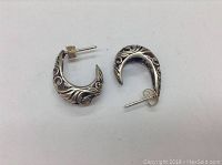 Pair of sterling silver stud earrings with curved filigree design shown from above on white background