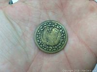 Reverse side of 1812 Wellington Canadian brass token with wreath-like dotted circle and central emblem.