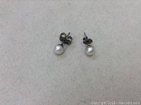 Pair of small pearl stud earrings on a light background showing tarnished silver posts and white pearls.