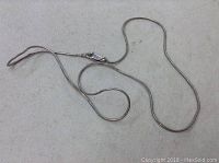 Full length view of the silver snake chain necklace laid out against a light gray background, showing its length and lobster clasp.