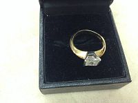 Gold plated ring with square-cut cubic zirconia stone in black jewelry box, side view.