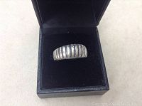 Front view of old silver sterling ring in black jewelry box, shows ribbed detailing and rounded profile.