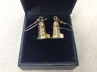 Pair of gold-tone lighthouse-shaped earrings shown inside a black jewelry box with a soft black interior.