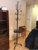 Full view of the tall black metal coat stand with vertical pole, several hooks at varying heights, and tripod base.