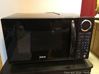 Front view of black RCA microwave showing door and control panel with keypad and dial