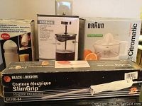 Photo showing four boxed kitchen appliances: Braun Citromatic juicer, Black & Decker electric knife, Stokes coffee maker, and Chasly hand and cheese grater.