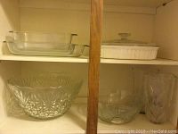 Two glass bowls and three pieces of rectangular bakeware inside a cabinet shelf.