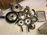 View of all stainless steel kettles, pots, skillets with lids, strainers and metal baking trays in the lot