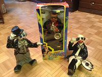 Three figurines on a parquet wooden floor: two clown figures and one boxed Jazzman figure.