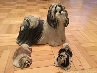 Front view of three dog figurines on wooden floor showing large long-haired dog and two smaller dogs