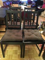 Four black wooden IKEA Stefan dining chairs with dark brown tufted cushions, set on parquet floor in living room.