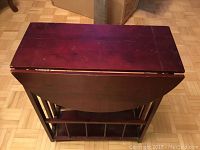 Folded wooden side table with dark cherry finish showing scratches and wear on top surface.
