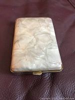 Closed view of the cigarette case showing the marbled plastic exterior with metal rim and chip on corner.