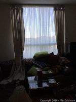 Beige drapes with sheer curtains hung over a large window in living room, sunlight visible through sheers