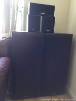 Five Technics speakers stacked and displayed against corner wall, two large floor-standing and three smaller speakers.