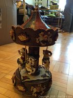Front view of the decorative merry go round showing painted carousel horses, figurines, and fabric floral decoration on the base and canopy.
