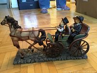 Side angled view of the horse-drawn carriage figurine highlighting the horse, carriage, and two seated figures.