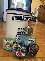 Photo showing the cookie jar with 3D Lucy figure and the three metal mint containers in front of it, placed on a wooden floor.