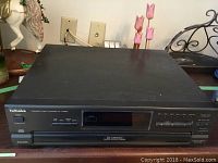 Front view of black Technics compact disc changer with power button and display screen on the front panel.