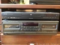 Front view showing Toshiba DVD player stacked on top of the Technics stereo cassette deck with visible buttons and display.