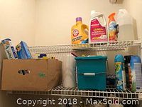 White metal wire shelving with assorted cleaning bottles including Arm & Hammer detergent and a cardboard box with food storage wraps, a blue plastic bucket below.