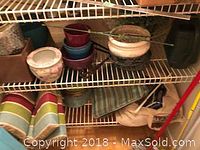 Wire shelving unit with various garden accessories visible, including multiple colorful pots, the artificial plant, watering can, cushions, bag of hangers, and other miscellaneous items.