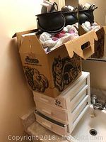 Photo of three drawer plastic storage unit with cardboard box on top containing assorted items