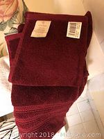 Two burgundy Ralph Lauren hand towels with original tags and a matching facecloth folded neatly.