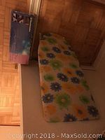 Mini ironing board with padded fabric cover featuring green, orange, and blue floral pattern, placed on wooden floor.