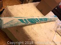 Rolled outdoor plastic woven rug placed on a bed, showing full length and rolled form.