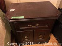 Front view of one bedside table showing the top surface, drawer with brass handle, and two cabinet doors with brass ring pulls.