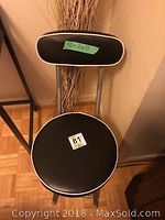 Top-down view of small black leatherette upholstered folding chair with metal frame, facing the backrest